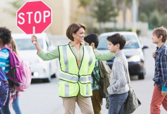 Female crossing guard who got her job through a staffing agency assists children to safely cross the street.